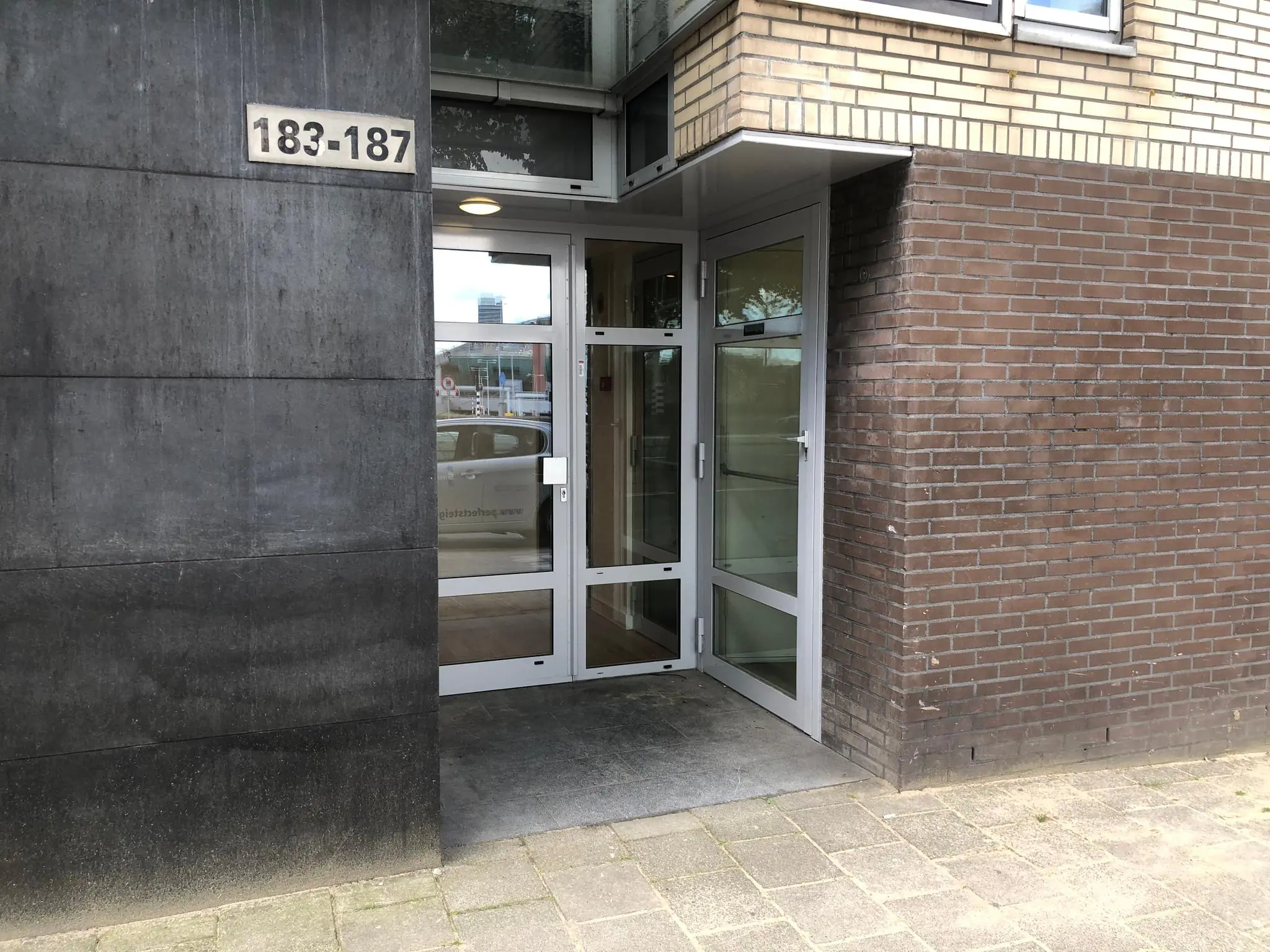 Ingang van een modern gebouw aan de Prins Hendrikkade met huisnummers 183-187.